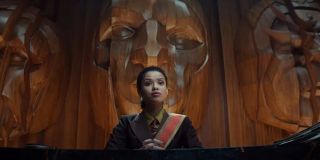 To ujęcie przedstawia nam wysoko postawioną urzędniczkę TVA, najprawdopodobniej sędzinę (TVA ma 6 sędziów rozstrzygających w sporach dotyczących m.in. „dobrej woli”, „pokoju” czy „wolności” – niejednokrotnie ci sędziowie sami łamią jednak własne zasady), w której rolę wcieli się Gugu Mbatha-Raw. Warto zwrócić uwagę na znajdujące się za nią twarze - te same, które widzimy na umiejscowionych w siedzibie TVA posągach. Nie jest wykluczone, że są one hołdem dla założyciela/założycieli organizacji. Część z komentatorów sądzi, że jedna z nich należy do Kanga Zdobywcy, ale jeszcze ciekawsze jest przypuszczenie, iż w tym przypadku mamy do czynienia z pomnikiem Living Tribunala, kosmicznej istoty stojącej na straży równowagi w całym multiwersum. Living Tribunal uznawany jest za 2. najpotężniejszą postać komiksowego uniwersum Marvela, zaraz po One-Above-All. Widzieliśmy go m.in. w słynnej „Rękawicy Nieskończoności”, w której mocarz zmierzył się z Thanosem.