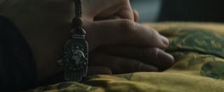 Umierająca kobieta ściska w ręku chamsę, używany w krajach bliskowschodnich symbol, znajdujący się w amuletach mających chronić przed złowrogimi siłami – zamiast charakterystycznego oka widzimy jednak kształt kuli ziemskiej. 